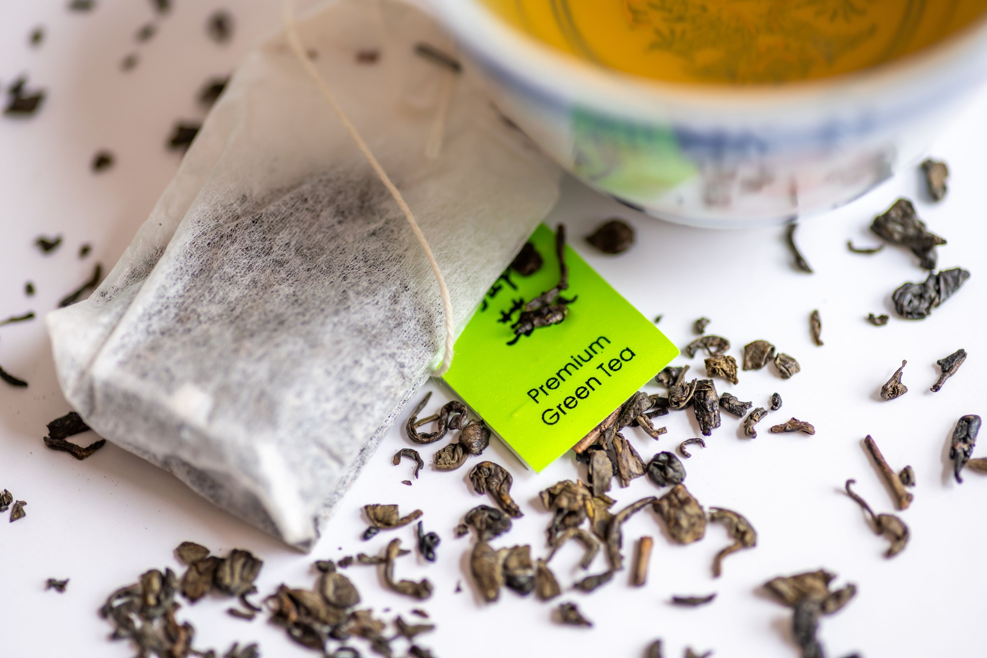 Loose green tea leafs and tea bags with a cup of green tea isolated in white. Health drink, healthy lifestyle concept.