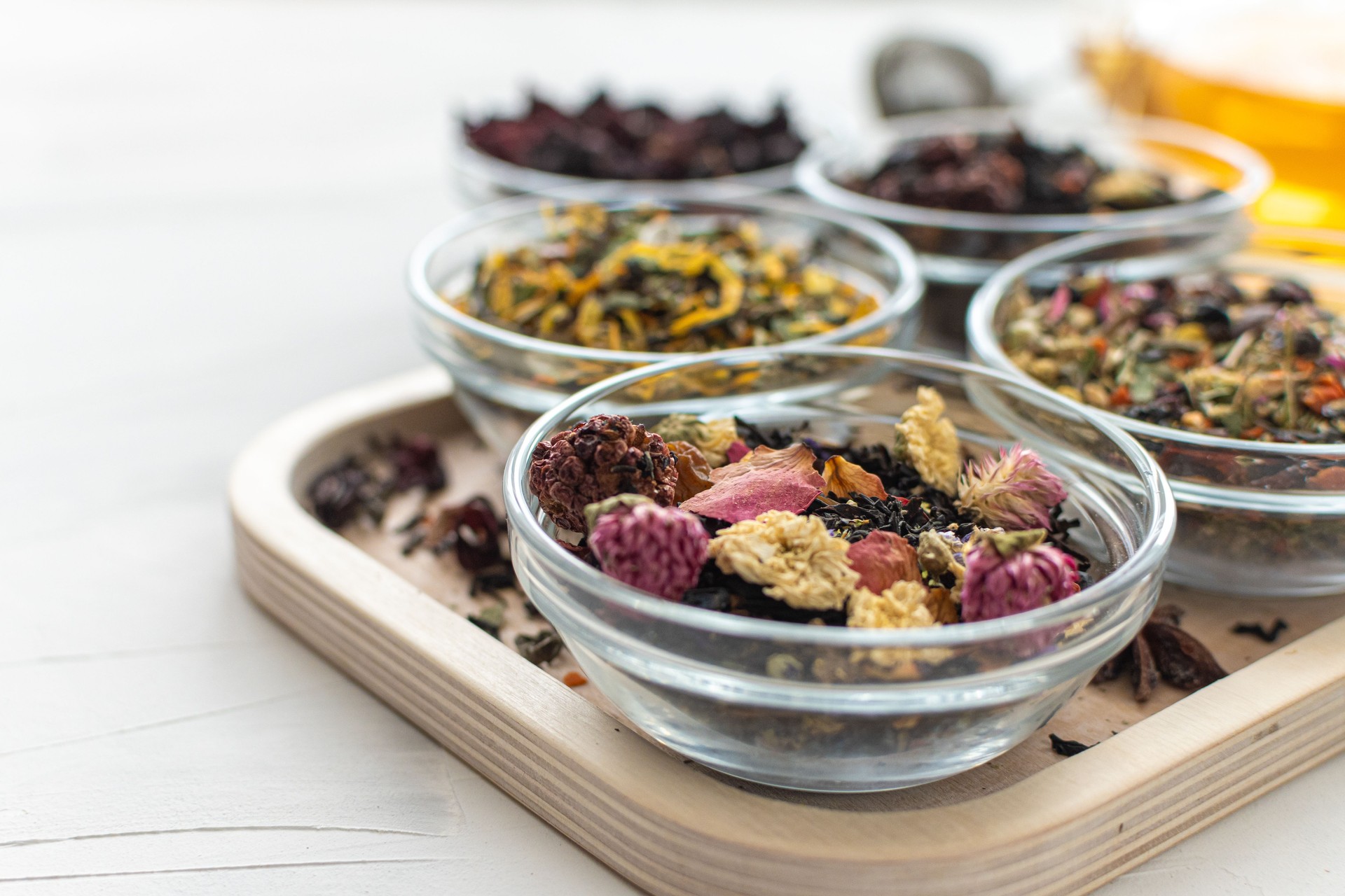 Different varieties of herbal green and black tea in glass bowls on a close-up tray. Selective focus. Herbal treatment. Healthy lifestyle. Therapeutic aromatic and delicious drinks. Space for text.